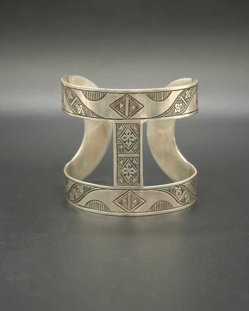 Close-up of a large, heavy, engraved Tuareg silver cuff bracelet, illustrating its minimalist, architectural design and use of geometric symbols.