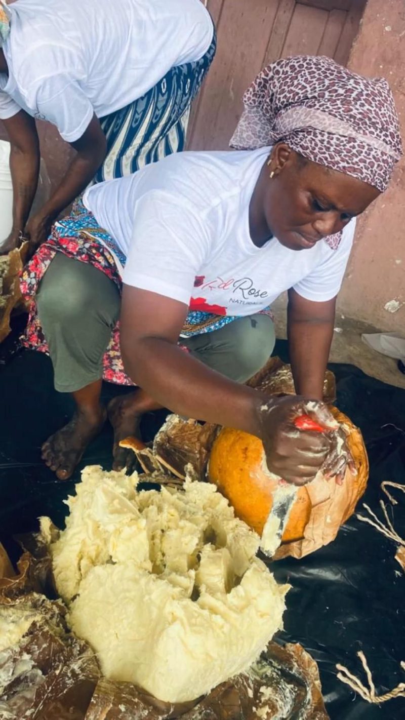 A woman scooping shea butter from a clay pot.
