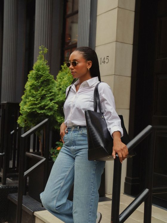 A woman carrying a leather tote bag in an outdoor setting.