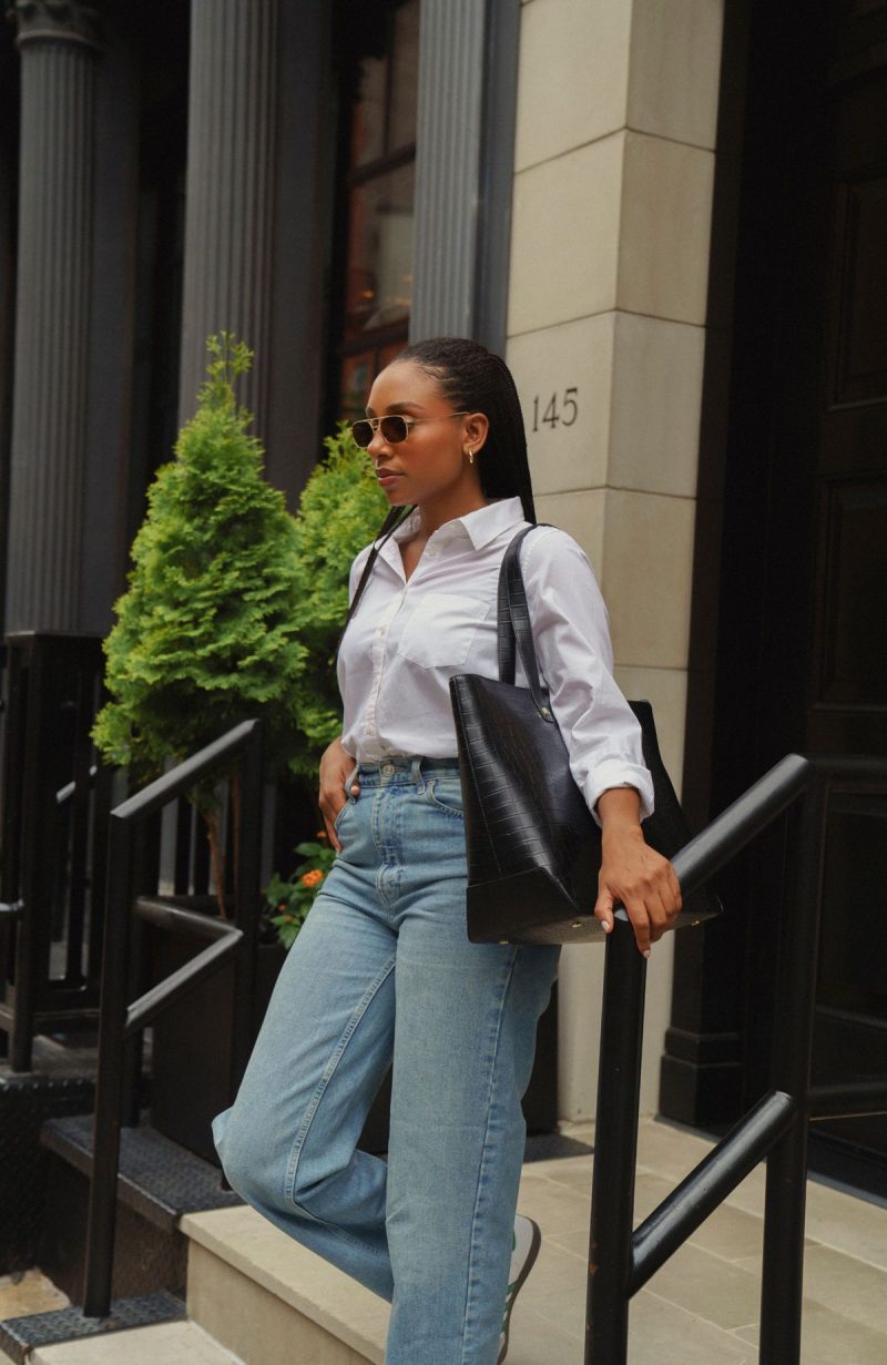 A woman carrying a leather tote bag in an outdoor setting.

