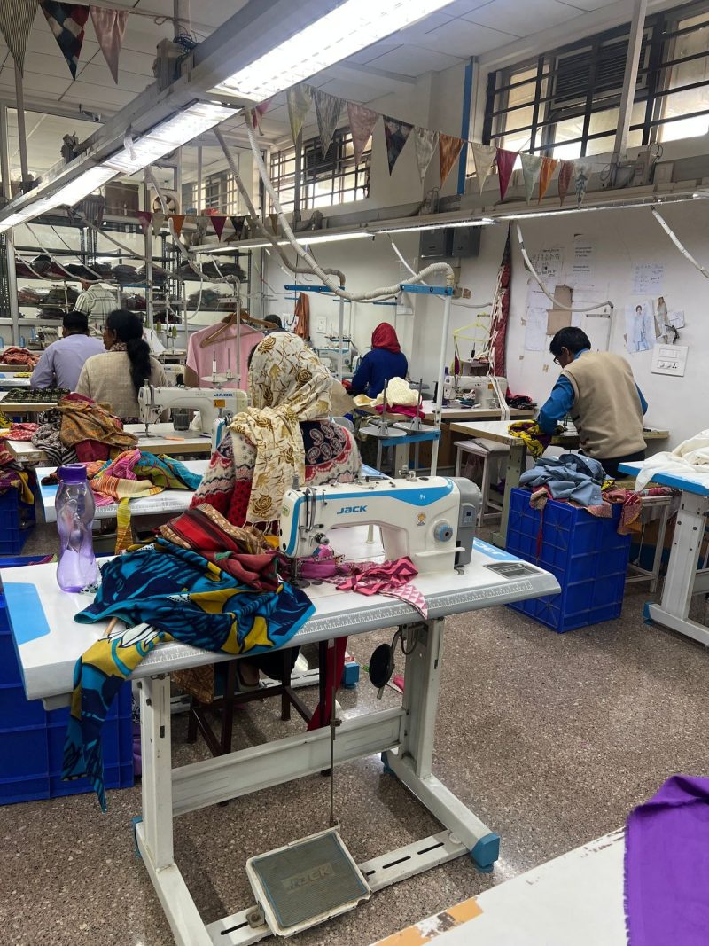 A bright, high-end African garment factory with staff working on luxury designs, shot in a documentary style to prove traceability and the commercial scale of the local fashion 