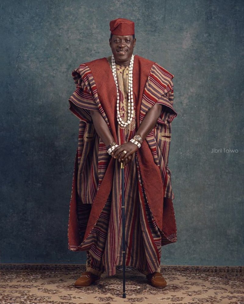 This is a full-length photograph of an African man wearing an embroidered agbada, which highlights the voluminous, structured royal silhouette of the outer robe and demonstrates the enduring influence of regal provenance on modern ceremonial attire.