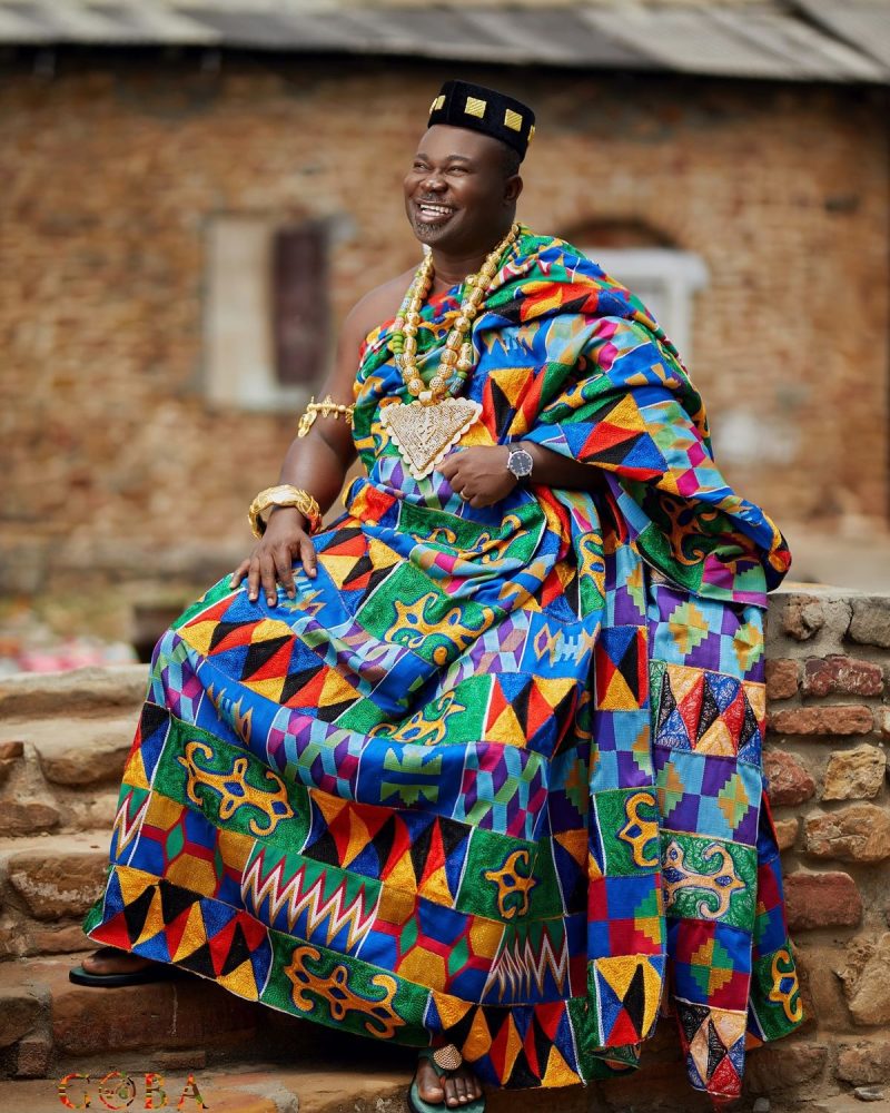 The image depicts a portrait of an African man meticulously draped in an Ewe Kente cloth, showcasing the vibrant geometric patterns and the ancestral craft of this ceremonial textile, which represents cultural provenance.