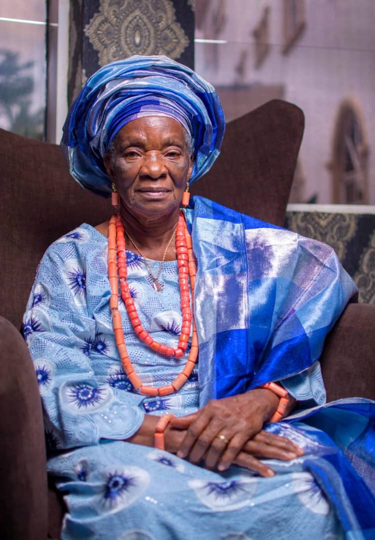 A picture of an elderly African grandmother seated gracefully in traditional blue attire and a headwrap.