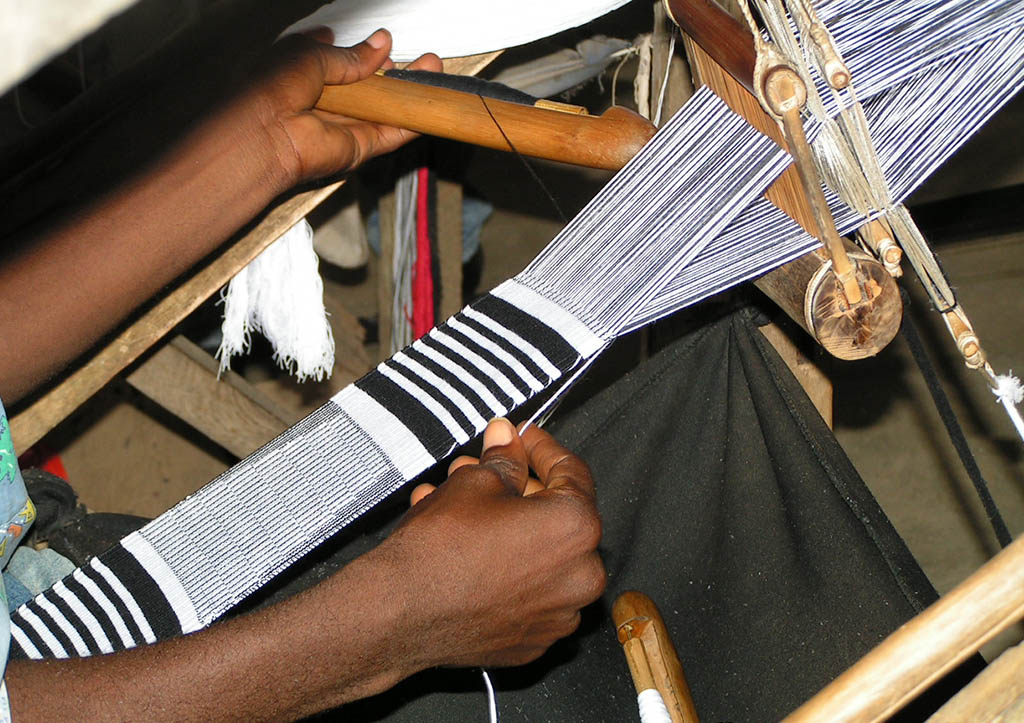 A picture of an Artisan in Bonwire weaving Kente on a narrow loom.
