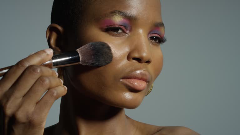 Portrait beautiful young dark skin female model with shave head in gold hoop earrings applying makeup  with brush