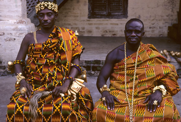 An image showing two older men draped in Kente sitting on a chair
