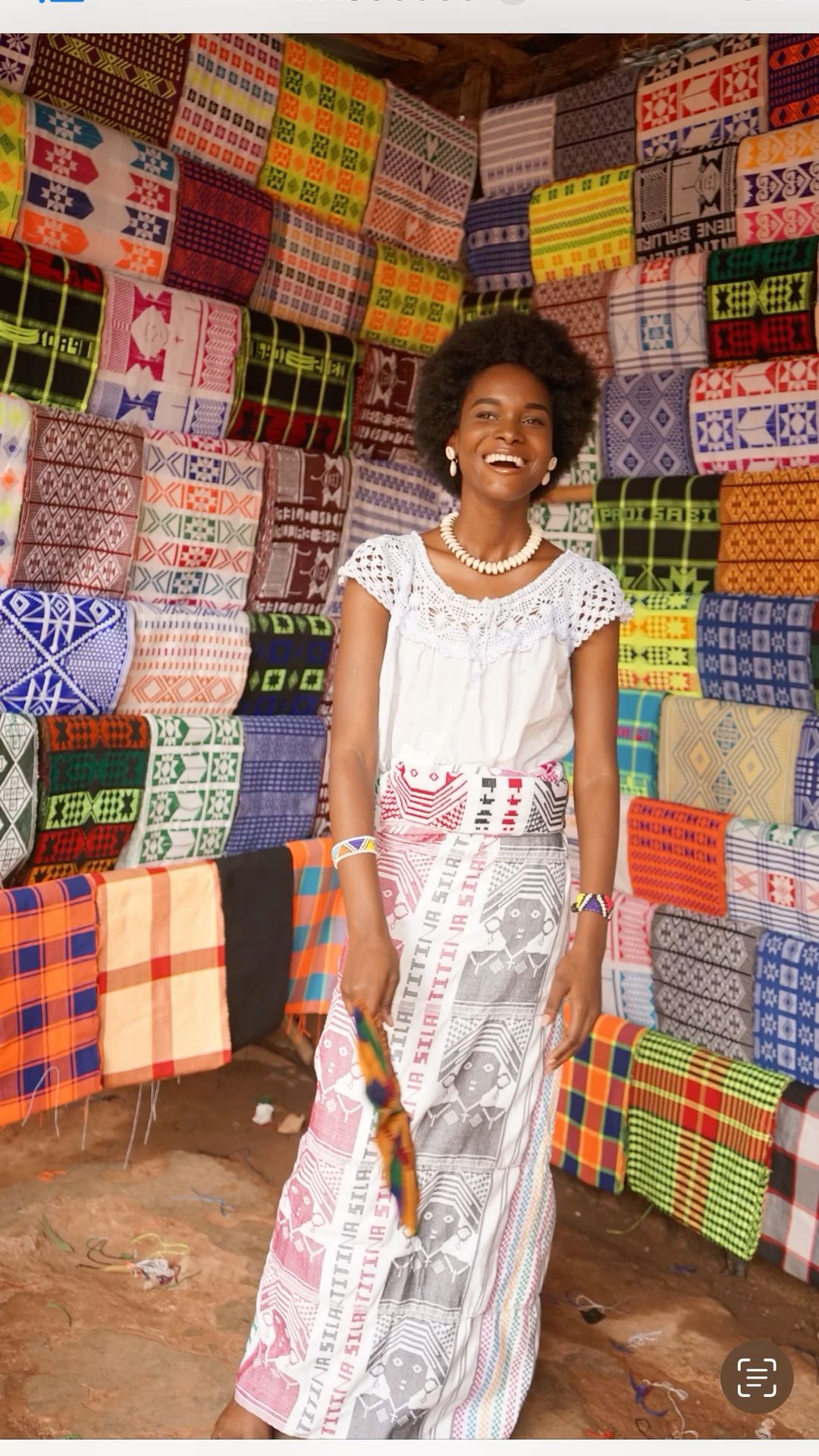 A young woman standing next to traditional wrappers and textiles in Guinea-Bissau.