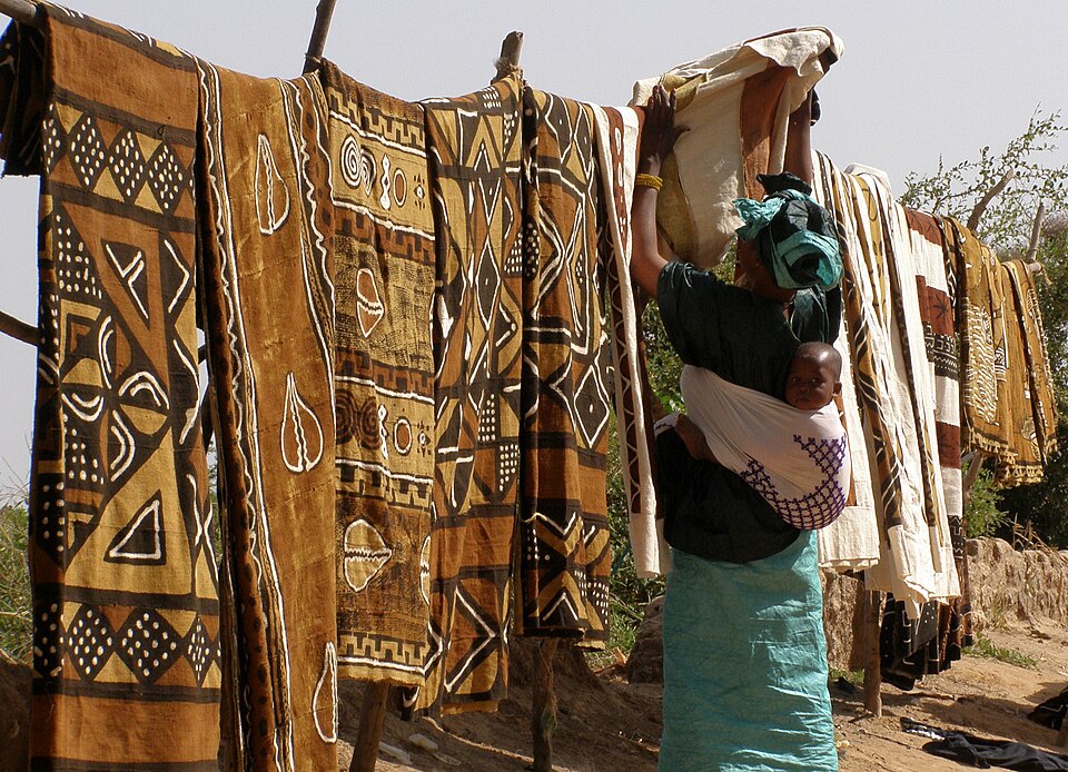 An image showing a lady with her baby standing in front of various bogolan fabrics