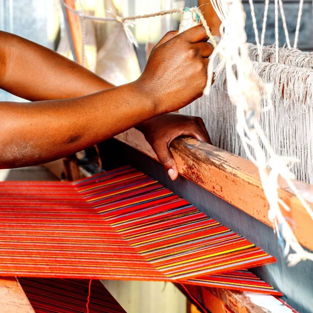 Artisan weaving African textiles on a traditional loom for craft fashion preservation.