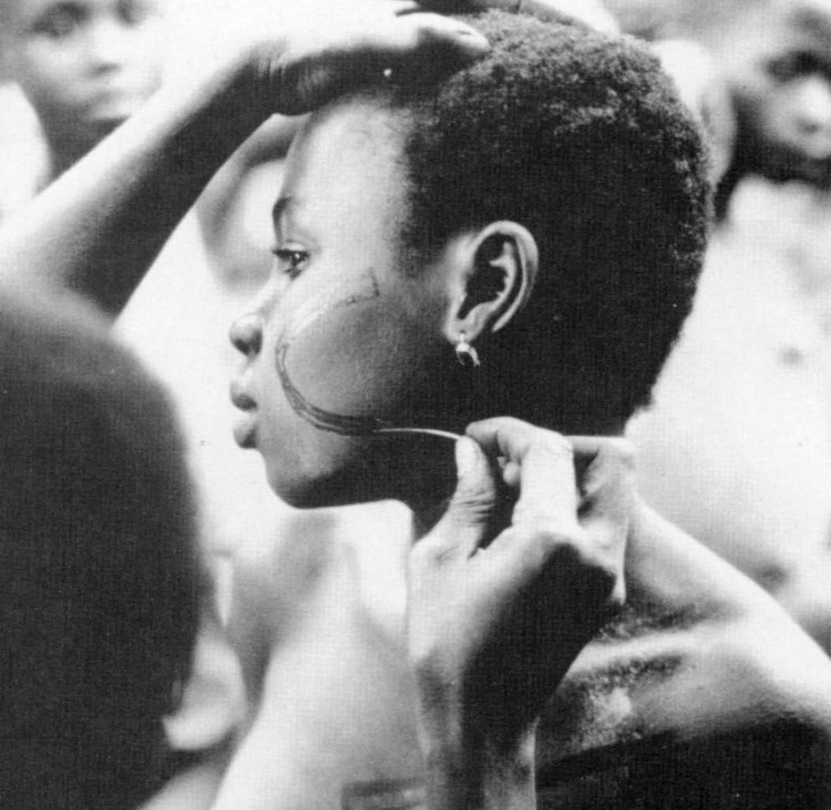 Igbo woman applying traditional Uli body art with fine plant-based dye during a communal beauty ritual.